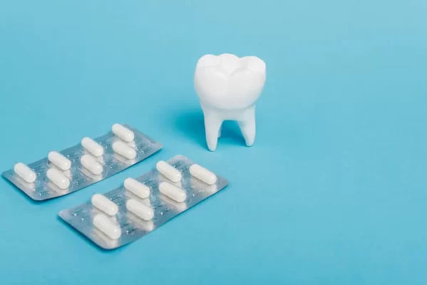 Close up view of blisters with pills and tooth model on blue background